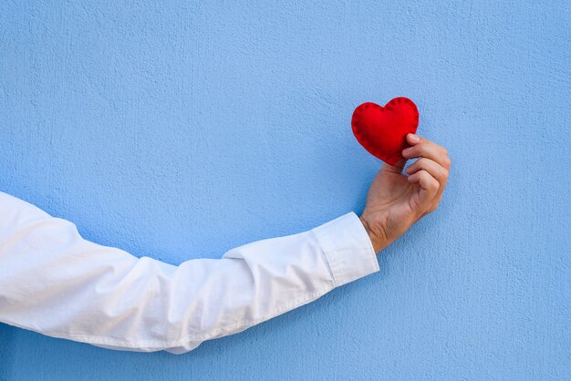 Foto valentinstagskarte. das rote herz in der hand des mannes gegen die blaue wand