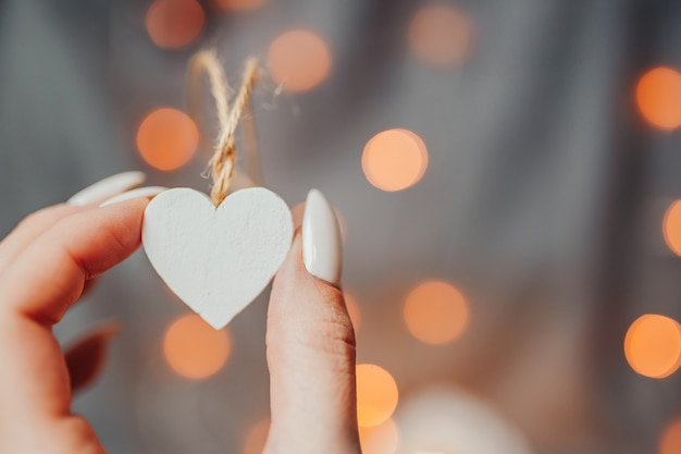 Valentinstagskarte. Frau hält viele weißen hölzernen Herzen auf dem hellen Hintergrund. Herzen mit Girlandenlichtern Bokeh.