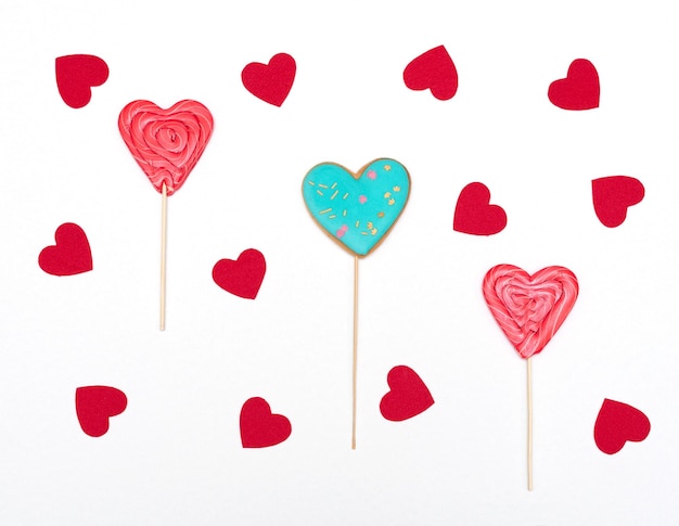 Valentinstagskarte mit herzförmigen Lebkuchen und Lutschern auf weißem Hintergrund mit roten Herzen Liebesurlaubskonzept Flacher Lay-Stil
