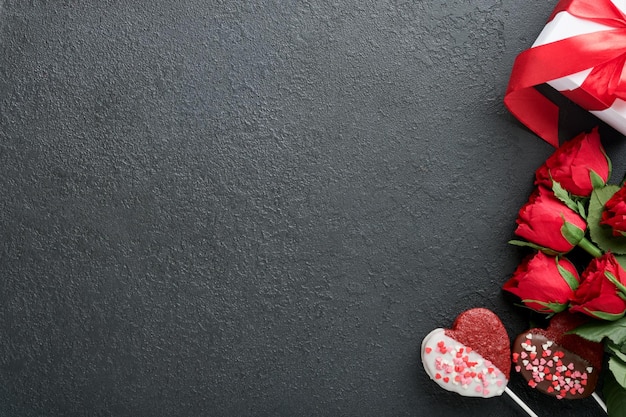 Valentinstagskarte Rosenrote Blumen, Brownie-Kekse und Pralinen auf herzförmiger Geschenkbox mit Wein auf schwarzem Hintergrund Grußkarte zum Mutter- oder Frauentag Draufsicht flach gelegt