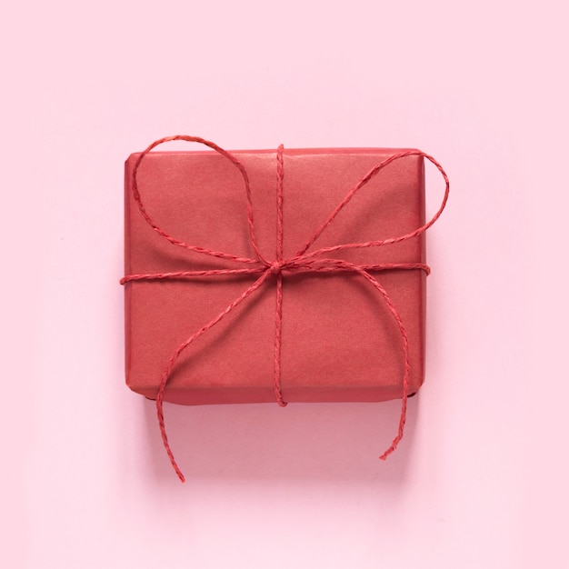 Valentinstagskarte. Rotes Geschenk mit Bogen des Seils auf Pastellrosa. Ansicht von oben.
