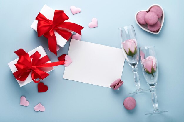 Valentinstagskarte. Weiße Geschenkboxen mit rotem Band, Sektflasche und Macaron-Makronen-Plätzchen auf blauem Hintergrund. 8. März, Valentinstag, Geburtstag der Mutter der Frauen. Attrappe, Lehrmodell, Simulation.