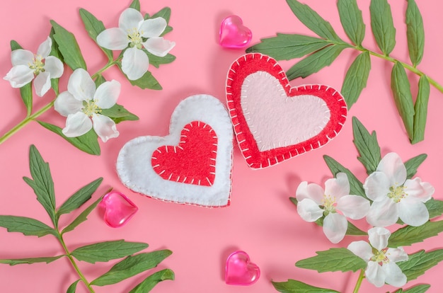 Valentinstagskarte, zwei Herzen mit einem Rahmen von Blumen und Blättern auf einem rosa Hintergrund