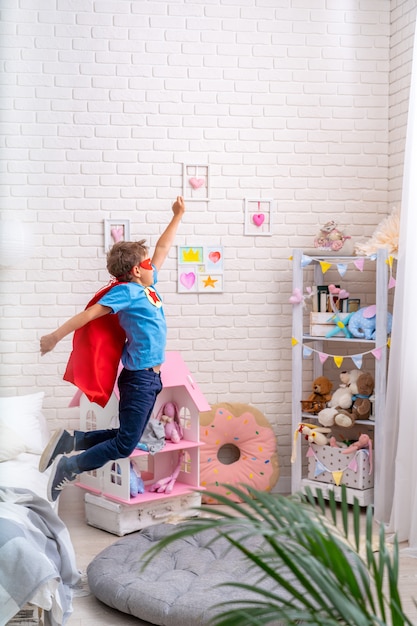 Valiente niño salta de la cama, imaginando el vuelo. niño juega superhéroe