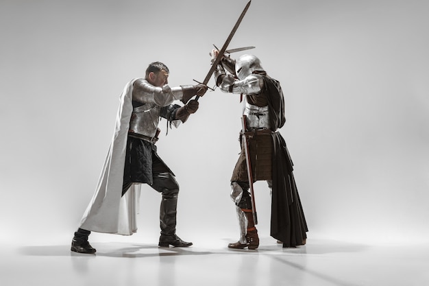 Valientes caballeros armados con armas profesionales luchando aislado sobre fondo blanco de estudio. Reconstrucción histórica de lucha nativa de guerreros. Concepto de historia, afición, arte militar antiguo.