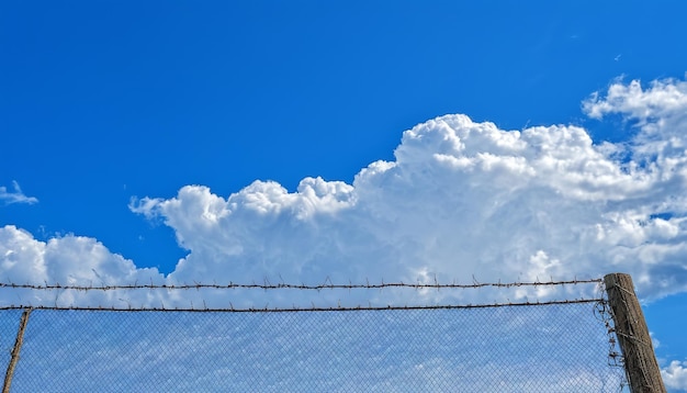 valla de alambre de púas con un cielo azul y nubes en el fondo