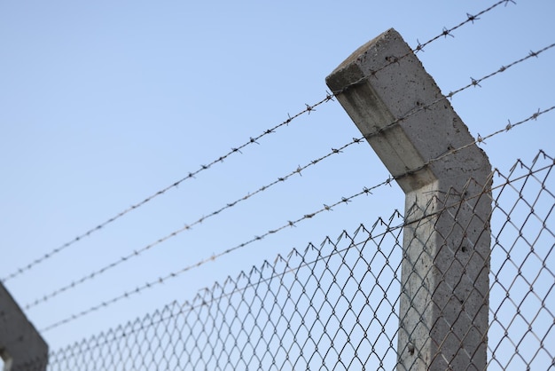 Valla de alambre de púas contra el muro de seguridad de la prisión de cielo azul o el concepto de zona militar