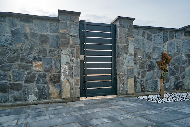 Valla alta de piedra con puerta de hierro cerrada en patio pavimentado de propiedad de diseño de estilo moderno al aire libre