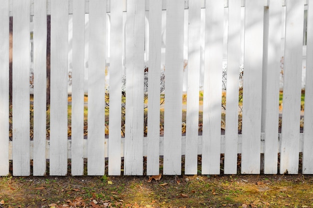 Valla blanca alta en frente de la casa en otoño con sombras de ramas.