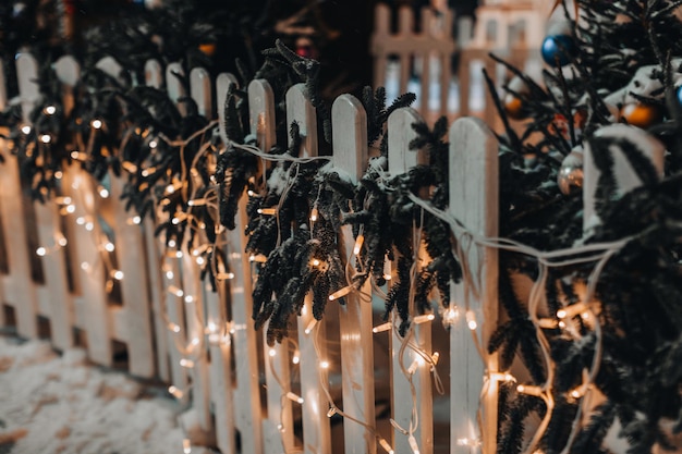 Valla de madera decorada con guirnaldas doradas y ramas de año nuevo en la nieve.