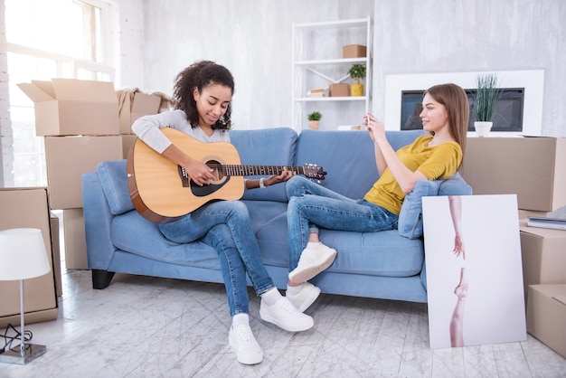 Foto valorar el talento. encantadora niña sentada en el sofá junto a su mejor amiga y filmando su guitarra en el teléfono