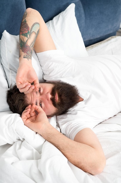 Vamos começar um novo dia Relaxe e durma conceito Homem barbudo dorme em lençóis brancos Sono saudável e bem-estar Homem barbudo moderno sonolento na cama Horas da manhã Insônia e problemas de sono