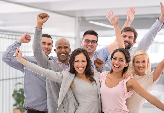 Vamos comemorar o sucesso. Foto recortada de um grupo de empresários sorrindo e levantando as mãos.