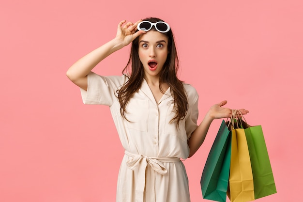 Vamos fazer compras. Viciada em compras feminina divertida e animada se divertindo navegando pelos shoppings da cidade, segurando sacolas de compras, tirando óculos, vendo exatamente o que estava procurando, parede rosa