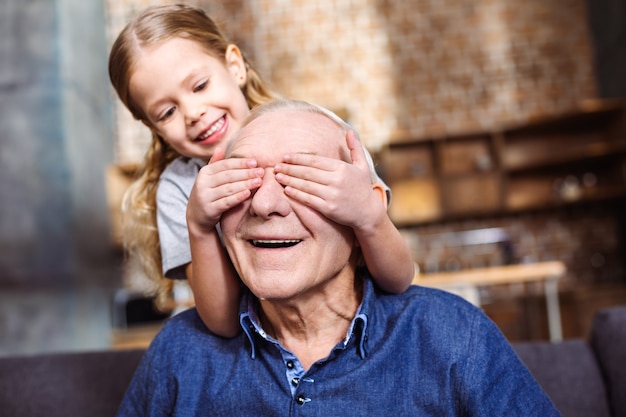 Foto vamos a jugar. linda niña sonriente cerrando los ojos de su abuelo mientras se divierte