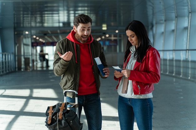 Vamos tarde. Joven barbudo sosteniendo boletos y gritando a su esposa mientras estaba de pie en el aeropuerto. Problemas durante el concepto de viaje