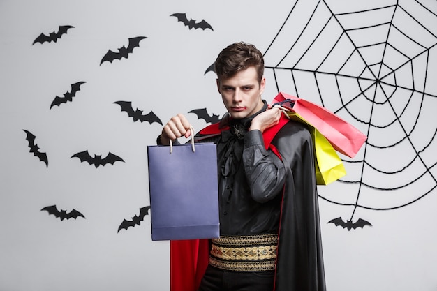 Vampir-Halloween-Konzept - Glücklicher schöner kaukasischer Vampir, der bunte Einkaufstasche hält.