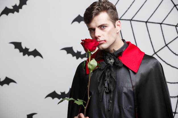 Vampire halloween concept - retrato de vampiro caucasiano bonito segurando rosa linda vermelha.