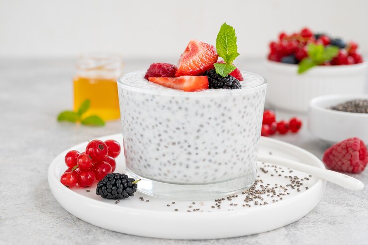 Vanille-Chia-Pudding mit frischen Beeren und Honig im Glas auf grauem Beton