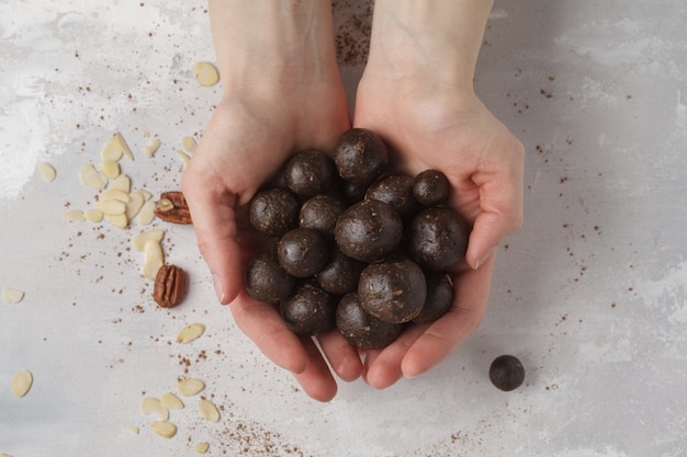 Vanille-Schokolade rohe vegane süße Kugeln mit Nüssen, Datteln und Kakao in den Händen. Gesundes veganes Lebensmittelkonzept. Grauer Hintergrund