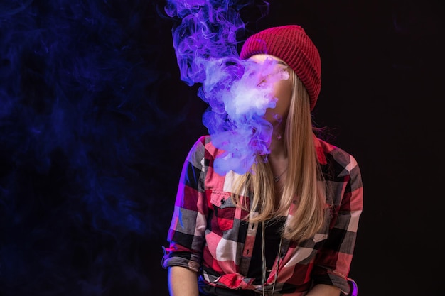 Vaping girl. Mulher jovem hippie vape e-cig no estúdio em fundo preto. Estilo hip-hop. Fechar-se.