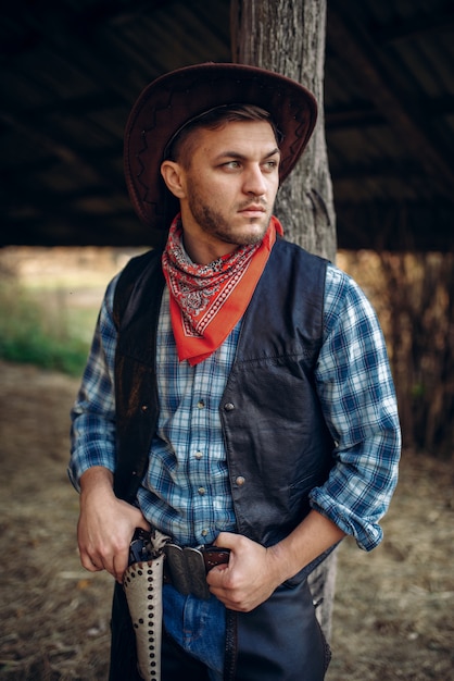 Vaquero brutal en jeans y chaqueta de cuero, rancho de texas, western. Persona del sexo masculino vintage con revólver, estilo de vida del salvaje oeste