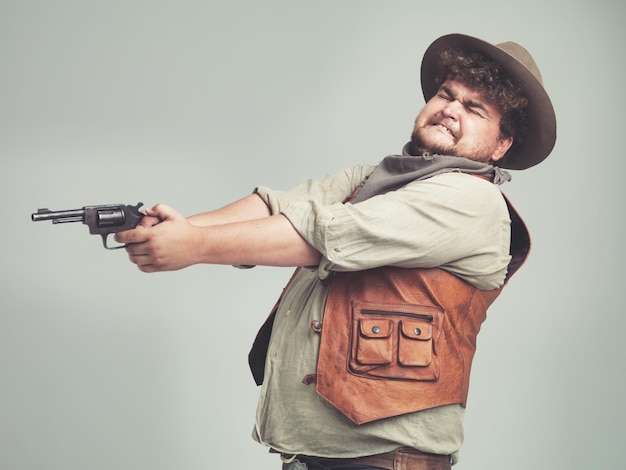 Vaquero hombre gracioso y arma de tiro en el estudio arma y pistola para la lucha occidental aislado en un fondo blanco criminal de tamaño plus y persona con revólver asustado o adivina apuntar con miedo en Texas