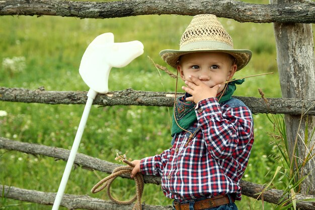 Un vaquero de niño con sombrero con cuerda cerca de la valla en la naturaleza