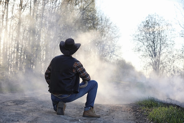 Un vaquero con sombrero y chaleco está de pie en medio de un espeso humo en la carretera