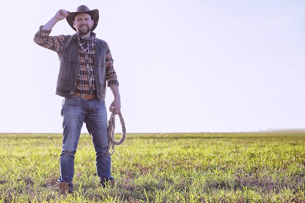 Vaquero con sombrero y un lazo de pie en un campo al atardecer