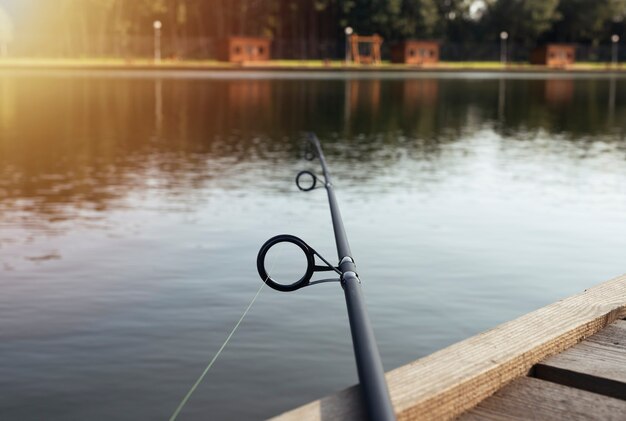 Vara de pesca deitada na costa de madeira ao longo do rio ou lago no verão