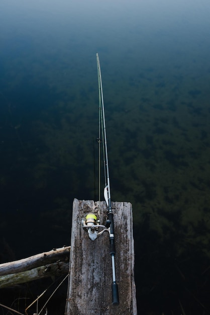 Vara de pesca em uma ponte no fundo da lagoa Girando com carretel no rio cais Manhã enevoada no lago natureza selvagem O conceito de recreação rural Artigo sobre dia de pesca Banner vintage para design