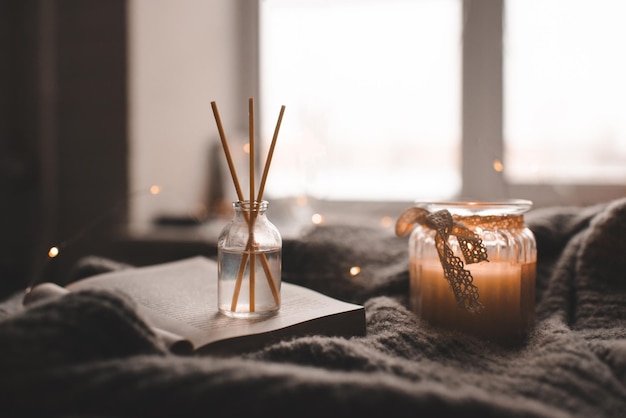 Varas de bambu em garrafa com velas perfumadas e livro aberto na bandeja de madeira na cama closeup. Aroma de casa. Aromaterapia.