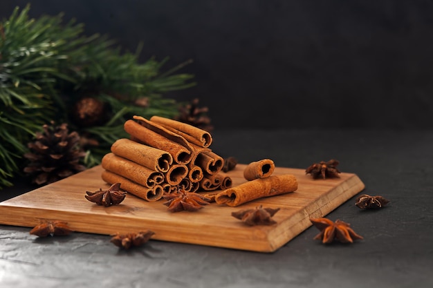 Varas de canela perfumadas com anis em uma placa de madeira em um fundo preto