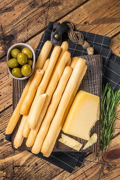 Varas de pão grissini tradicional aperitivo italiano na placa de madeira com azeitonas e queijo parmesão Bakground de madeira Vista superior