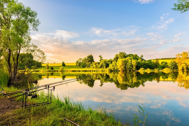 Varas de pesca na margem do rio calmo ao pôr do sol