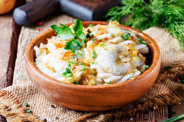 Vareniki russo tradicional com batatas e cebolas fritas em tigela na velha mesa de madeira estilo rústico foco seletivo