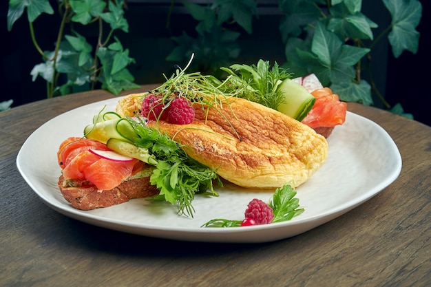 Variação de smorrebrod em pão de centeio com omelete, pepino e salmão em um prato branco sobre uma superfície de madeira