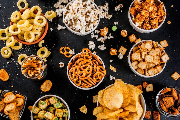 Variação diferentes biscoitos salgadinhos insalubres, pipoca salgada doce, tortilhas, nozes, palhas, bretsels