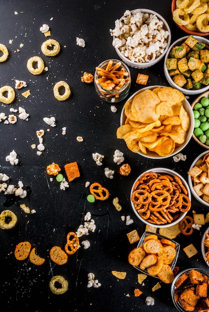 Variação diferentes biscoitos salgadinhos insalubres, pipoca salgada doce, tortilhas, nozes, palhas, bretsels