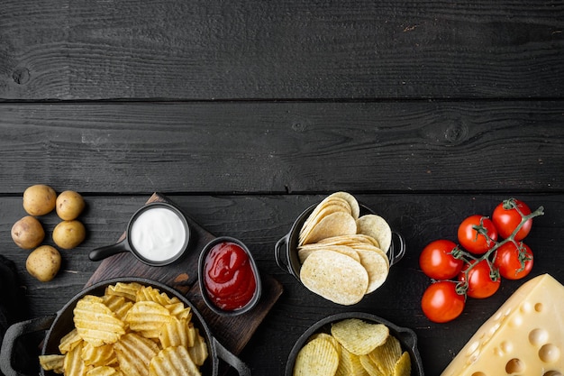 Variación de diferentes papas fritas con queso y cebolla sobre fondo de madera negra vista superior plana con espacio de copia para texto