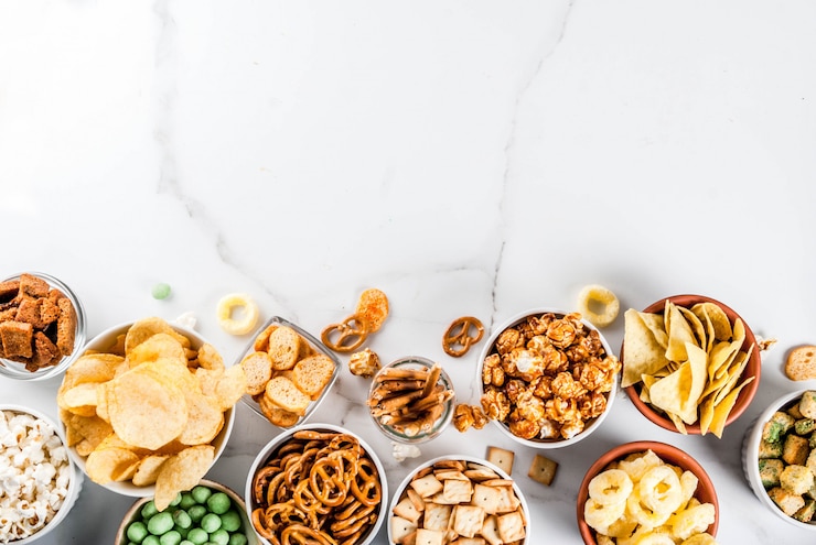 Foto variación de diferentes refrigerios poco saludables galletas saladas, palomitas de maíz saladas dulces, tortillas, nueces, pajitas, bretsels, fondo de mármol blanco copia espacio refrigerios saludables