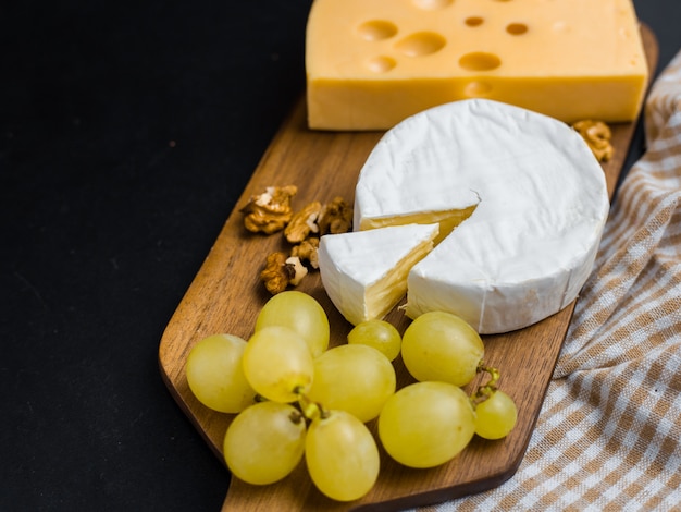 Variación de queso, nueces y uvas en tabla de cortar de madera. Queso Camembert y queso Edam. Comida para vino y romántica, desde la vista superior.