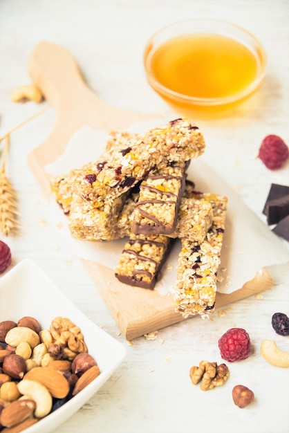 Varias barras de granola caseras con nueces, semillas, chocolate negro, miel y bayas sobre una tabla de madera