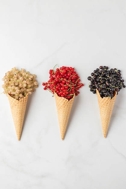 Varias bayas de grosella en conos de helado de waffle en mármol blanco. Grosella roja, negra y blanca. vista superior