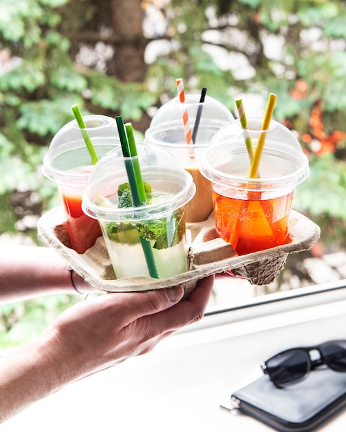 Várias bebidas geladas de verão e coquetéis em um suporte de papel nas mãos masculinas