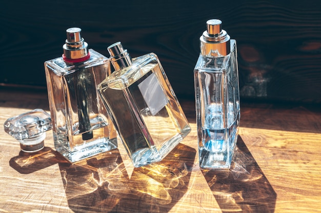 Varias botellas con perfume en rayos de sol sobre mesa de madera