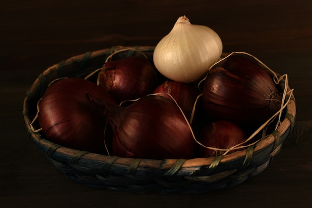 Varias cabezas de cebolla roja española y uno blanco doblado en una cesta de mimbre