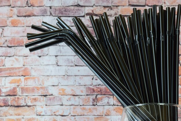 Varias docenas de tubos de cóctel negros decorativos en un vaso contra un fondo de pared decorativa de ladrillo