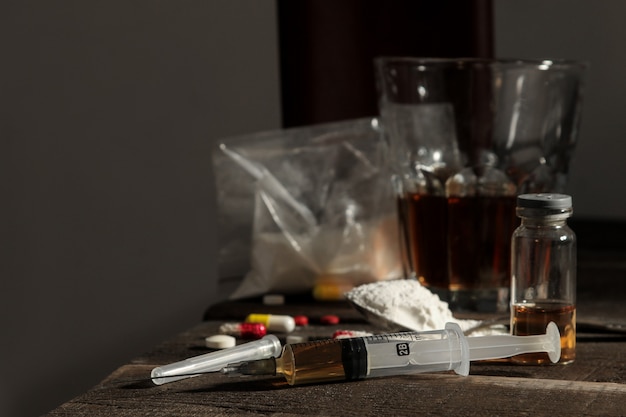 Varias drogas adictivas como alcohol, cigarrillos y drogas en una mesa de madera marrón. Concepto de adicción a las drogas